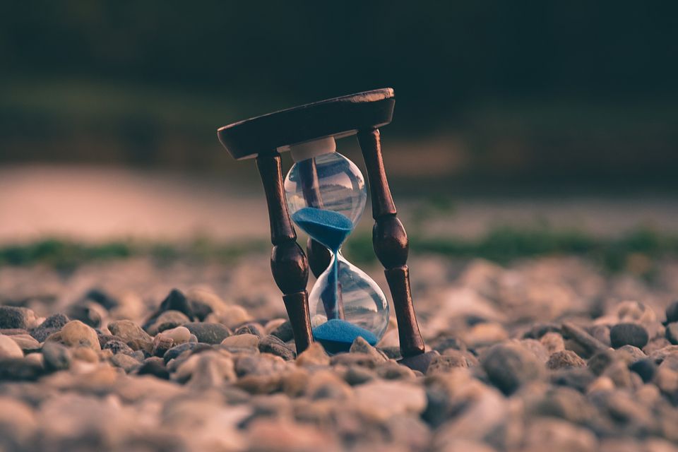 A sand timer is sat on a pebble beach as blue sand filters through