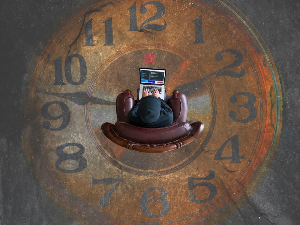 Person sits on leather armchair with a laptop balanced on their lap. On the floor is a large clock painted on the floor.